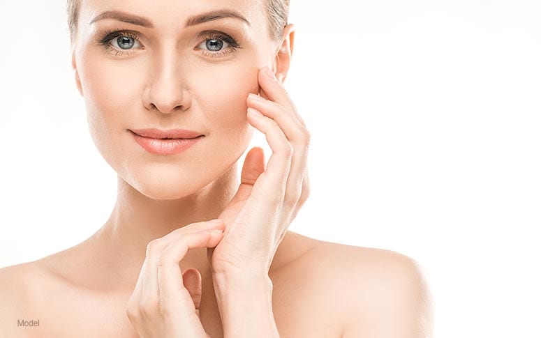 younger woman with bright and clear skin touching her face with one hand