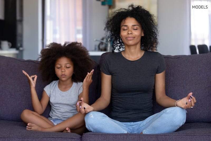 Young mother meditating with her daughter on the couch.