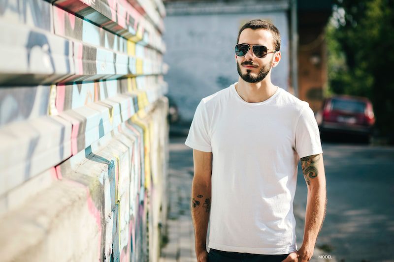 Young man in white shirt standing beside wall with graffiti